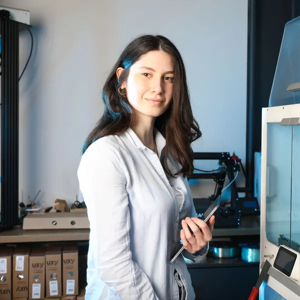 A young engineer beside a 3D printer, holding a tablet